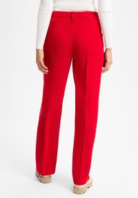 Rode, wijde pantalons met een gladde textuur en een elastische tailleband, voorzien van zijzakken en een relaxte pasvorm, gecombineerd met beige platform sandalen.