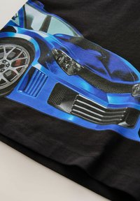 Grafică cu un automobil sportiv albastru, având roata din față detaliată, farurile și grila imprimate pe un material textil negru.