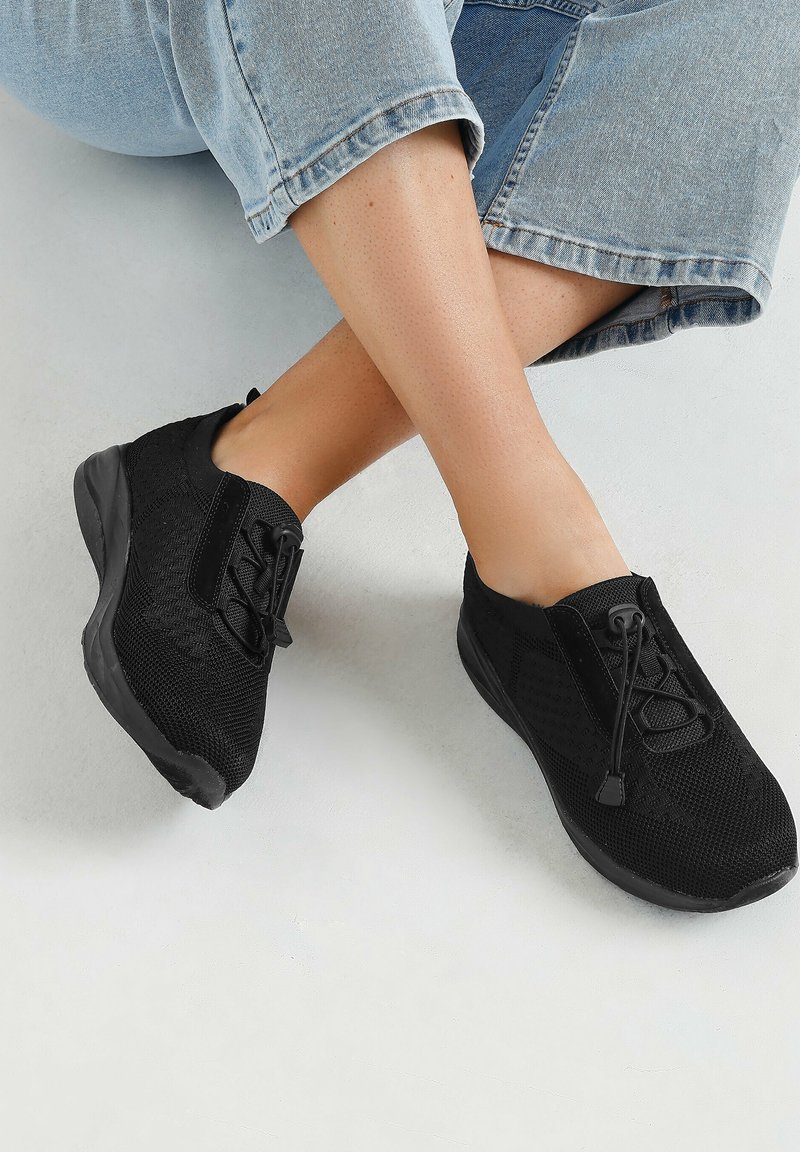 Zwarte sportieve schoenen van mesh materiaal, met een vetersluiting, rubberen zool en een gestructureerde bovenkant voor ademend vermogen en comfort.