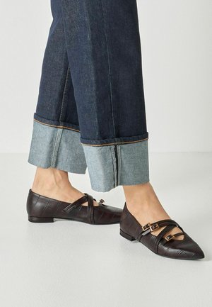 Person, die dunkelblaue Jeans mit weitem Umschlag und dunkelbraune spitze Ballerinas mit drei Schnallen trägt.