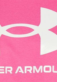 Camiseta de algodón rosa brillante con un gran logo blanco de Under Armour y texto. La tela tiene una textura suave y lisa.