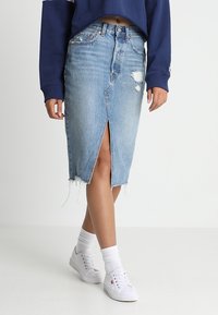 Jeans midi kjol med en främre slits, fransade kanter och slitna detaljer. Kombinerad med en marinblå kortärmad tröja och vita sneakers.