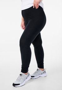 Mustad retuusid venivast kangast, millel on kroolitud disain ja sile tekstuur. Sobitatud hallide spordijalatsitega.