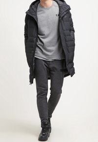 Schwarze Pufferjacke mit Kapuze, grauer Sweatshirt und dunkle Jogginghose. Enthält ein kleines Nike-Logo auf der Brust. Schwarze Sneakers.