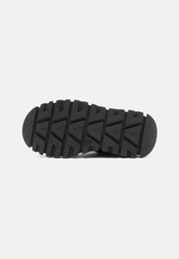Suela de zapato de goma negra con un patrón texturizado y resistente que presenta formas triangulares y rectangulares para mayor tracción. Diseño de punta redonda y plana.