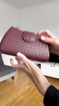 Bordo clutch torba napravljena od teksturirane kože s kopčom, koja ima suptilan uzorak dijamanta i zaobljene rubove.
