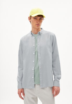 Lichtgrijs overhemd met knopen over een mintgroene t-shirt, gecombineerd met een heldergele pet. Eenvoudig ontwerp, lange mouwen, casual pasvorm.