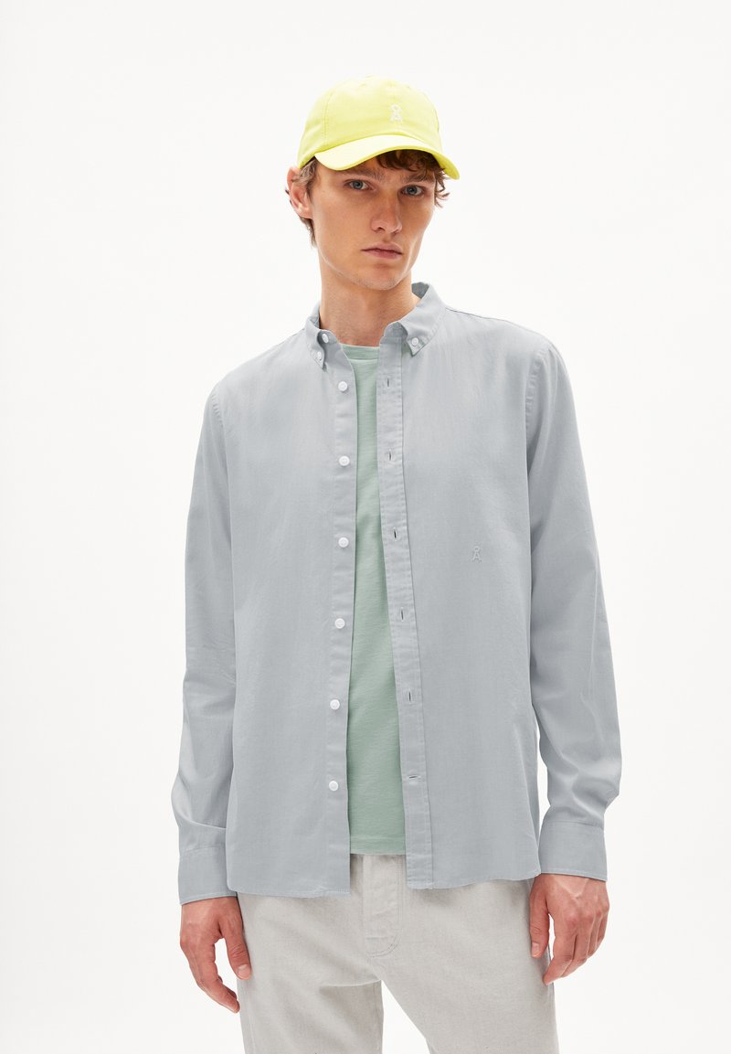 Lichtgrijs overhemd met knopen over een mintgroene t-shirt, gecombineerd met een heldergele pet. Eenvoudig ontwerp, lange mouwen, casual pasvorm.