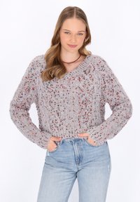 Pulover gri tricotat cu decolteu în V, având fire multicolore, mâneci lungi și tiv ribbed, asortat cu blugi deschiși la culoare, cu talie înaltă.