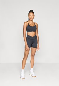 Top corto sportivo nero e pantaloni corti a vita alta realizzati in tessuto elasticizzato. Il design presenta una vita incrociata e cuciture minime.