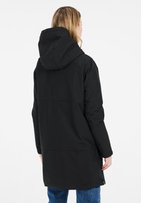 Veste noire à capuche au design mi-long, texture lisse, zips sur les côtés et un détail de couture dans le dos. Matériau léger.