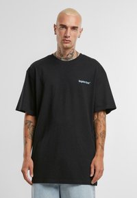 Fekete pamut póló rövid ujjakkal, kerek nyakkal, és egy kis fehér logóval a bal mellrészen. Világoskék farmernadrággal viselve.