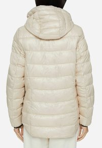 Chaqueta acolchada beige con capucha, que presenta secciones acolchadas horizontales y una textura suave y brillante. La parte posterior muestra un corte holgado y una capucha ajustable.