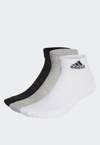 Tres pares de calcetines cortos en negro, gris y blanco. Cada uno cuenta con puños acanalados y el logo de Adidas en el calcetín blanco.