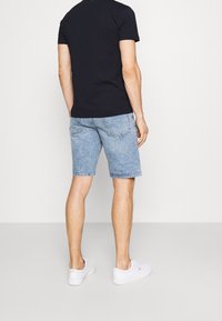 Jasnoniebieskie szorty dżinsowe o prostym kroju, z postrzępionymi brzegami i tylnymi kieszeniami, połączone z dopasowaną czarną koszulką i białymi sneakersami.