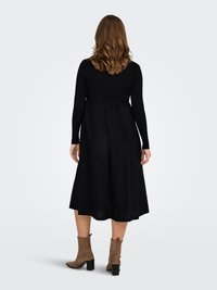 Czarna sukienka z długim rękawem, dopasowanym gorsetem i rozkloszowaną spódnicą, zestawiona z brązowymi, teksturowanymi botkami za kostkę. Prosta, elegancka sylwetka.