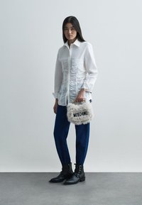 Valge kogulik pika varrukaga särk, tumel sinised kitsenevad teksad, mustad pahkluu saapad pandlatega ja pehme hall käekott tekstiga "MOSCHINO".