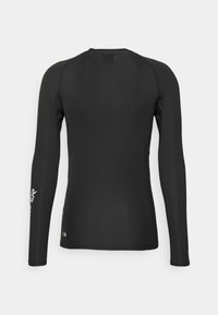 Camiseta atlética de manga larga negra, fabricada con una tela elástica. Presenta un escote redondeado y un pequeño detalle de logo en la manga izquierda.