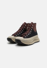 Vysoké boty s hnědým, semišovým svrškem a černými plátěnými stranami, s béžovou gumovou podrážkou a texturovaným gripem.