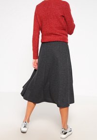 Pull en tricot rouge avec une finition texturée associé à une jupe noire en forme de A. Des baskets argentées complètent la tenue.