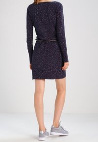 Marineblå klänning med långa ärmar, prydd med ett strukturerat mönster i rosa och vitt. Ett tunt bälte framhäver midjan. Matchas med grå sneakers.