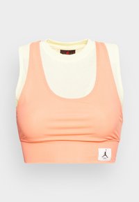 Stanik sportowy z brzoskwiniowej siateczki, o dopasowanym kroju, okrągłym dekolcie oraz białej metce z logo w dolnym lewym rogu.