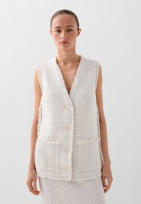 Mouwloos, crème tweed vest met een gestructureerd patroon, franjes en twee voorzakken, met drie knoopsluitingen.