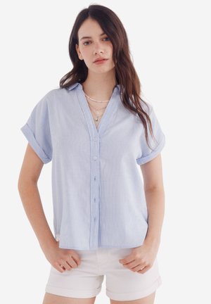 Light blue striped short-sleeve button-up shirt with a collar, relaxed fit, and rolled sleeves, paired with white shorts.
