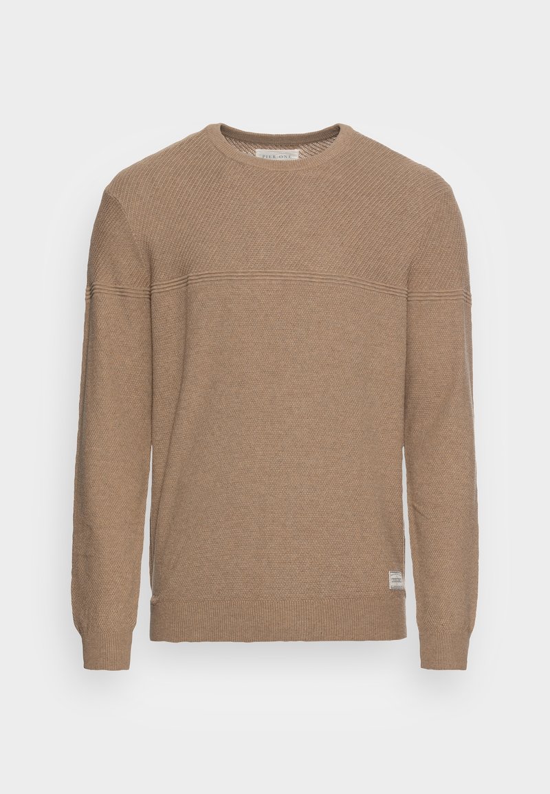 Beige neulepaita pyöreällä kaula-aukolla, teksturoidulla kuviolla, resorilla varustetut hihansuut ja helma. Sivussa pieni brändilaatta.