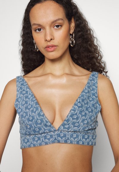 Blue patterned crop top made of denim, featuring a deep V-neck, wide straps, and a fitted design with intricate abstract motifs.