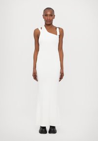 White, ribbed maxi dress with an asymmetrical neckline, one shoulder strap featuring accents. The model wears black, chunky boots.