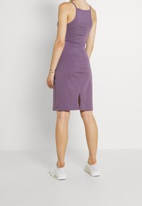 Lila kroppsnära klänning med slits bak, gjord av mjukt tyg, med tunna band och en elegant, enkel design. Bärs med vita träningsskor.