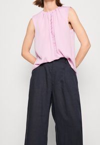 Top sin mangas de color rosa con un detalle fruncido en la parte frontal, combinado con pantalones anchos de pierna ancha de color azul marino oscuros y holgados. Textura de tela suave en todo.
