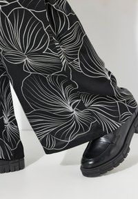 Wijde broek van zwarte stof met witte bloemmotieven, gecombineerd met chunky zwarte loafers met een gladde afwerking.