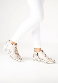 Stivaletti alla caviglia in beige chiaro con motivo in pelle di serpente, con zip laterale, suola in gomma con strisce bianche e texture liscia.
