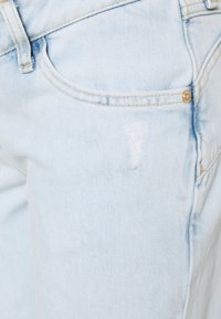 Jeans de ganga azul claro com um design clássico, apresentando uma área distressed e detalhes em metal dourado na cintura e nos bolsos.