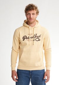 Felpa giallo chiaro con cappuccio e lacci, tasca frontale e testo grafico marrone. Tessuto morbido, maniche lunghe e polsini a costine sulla parte inferiore.