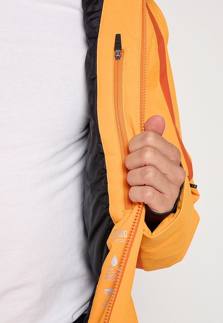 Pomarańczowa wodoodporna kurtka z czarnym wykończeniem, z zamykaną na zamek kieszenią na piersi oraz napisem informującym o detalach wodoodporności.