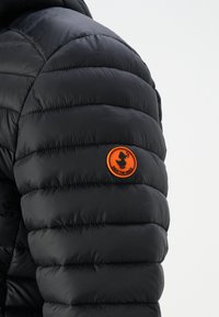 Svart polstret jakke med quiltet design og blank overflate. Har et oransje rundt logo merke med teksten "SAVE THE DUCK."