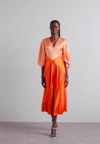 Midiklänning i orange satin med V-ringning och puffärmar. Kjolen flödar mjukt och skapar en smidig silhuett.