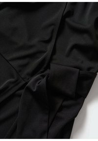 Vêtement noir à manches longues avec détail de revers plié, présenté en gros plan sur une surface plane avec la texture et les plis du tissu visibles.