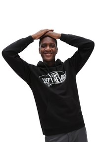 Sudadera negra con un bolsillo frontal, presenta un logo gráfico blanco. El material parece suave, con capucha ajustable y puños de canalé.
