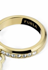 Prsten z zlatnog tona s glatkom, sjajnom završnom obradom, ukrašen prozirnim kristalima duž trake. Sadrži ugravirani natpis "Furla" na unutrašnjosti.