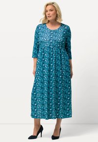 Teallinen polvipituinen mekko, jossa on 3/4-hihat, rypytetty vyötärö ja ympyräpilkku kuvio. Valmistettu kevyestä, lippuvasta kankaasta.