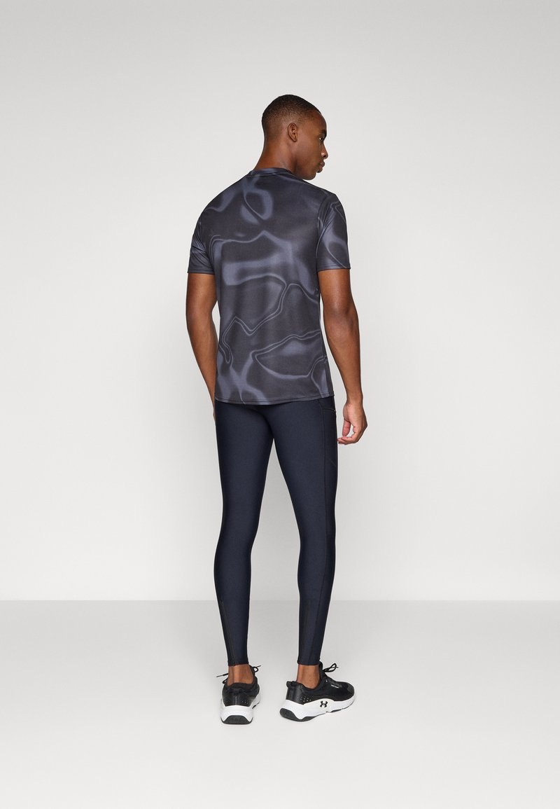 Korte mouwen, donkergrijs sportshirt met een vloeiend patroon, gecombineerd met strakke zwarte leggings en zwarte sportschoenen.