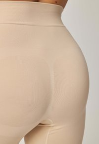 Beżowe leginsy z wysokim stanem wykonane z gładkiego, elastycznego materiału, charakteryzujące się bezszwowym krojem i subtelną teksturą dla wygody i dopasowania.