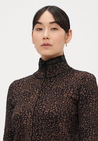 Čierny a hnedý leopardí vzor na topu na zips s vysokým golierom a pásom s logom na krku. Hladká látka s priliehavým strihom.