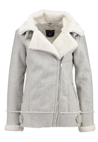 Veste grise avec un col et une doublure en fausse fourrure, fermeture éclair et tissu texturé. Présente des accents de sangle au niveau des poignets et des côtés.