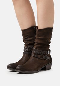 Braune Stiefeletten aus Kunstleder mit einem lässigen Schaft, geflochtenen Akzenten, seitlichem Reißverschluss und Blockabsatz. Strukturierter Stoff mit matter Oberfläche.