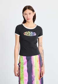 Sort T-shirt med korte ærmer og en hvid rund halsudskæring, med et flerfarvet "Adidas" logo. Sammen med en flerfarvet stribet nederdel.